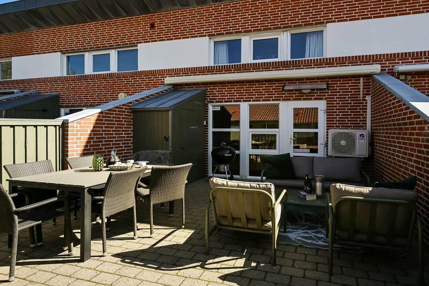 Terrasse mit Sitzgruppe, Tisch und Grill vor einem Backsteinhaus.