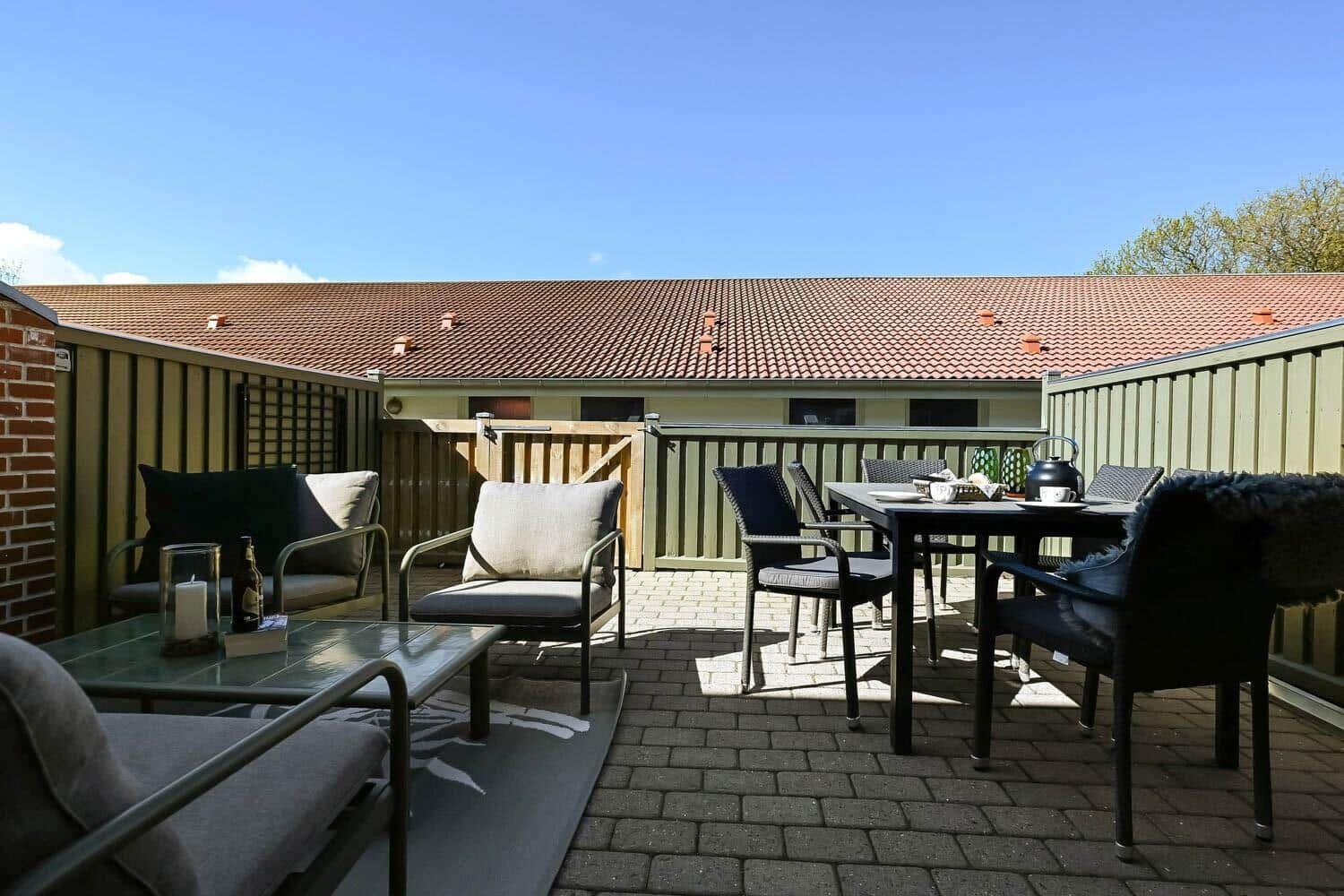 Terrasse mit Sitzgelegenheiten und Tisch. Hintergrund: Gebäude mit Ziegeldach.