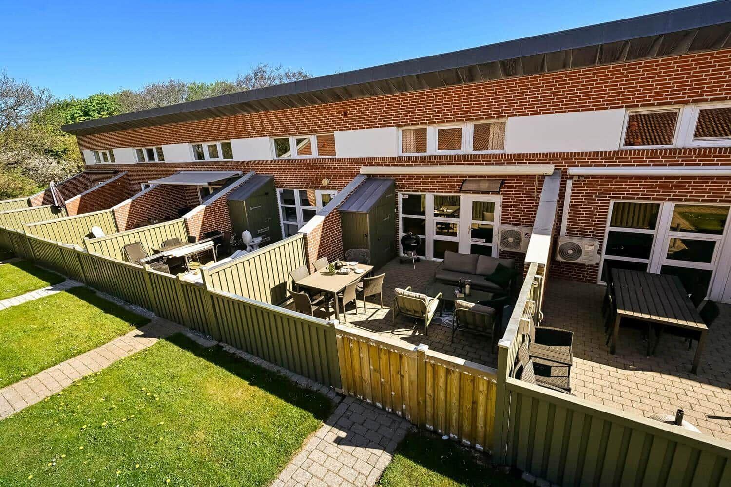 Rotes Backsteingebäude mit Terrassen und Gartenbereich. Außengelände mit Tischen und Stühlen.