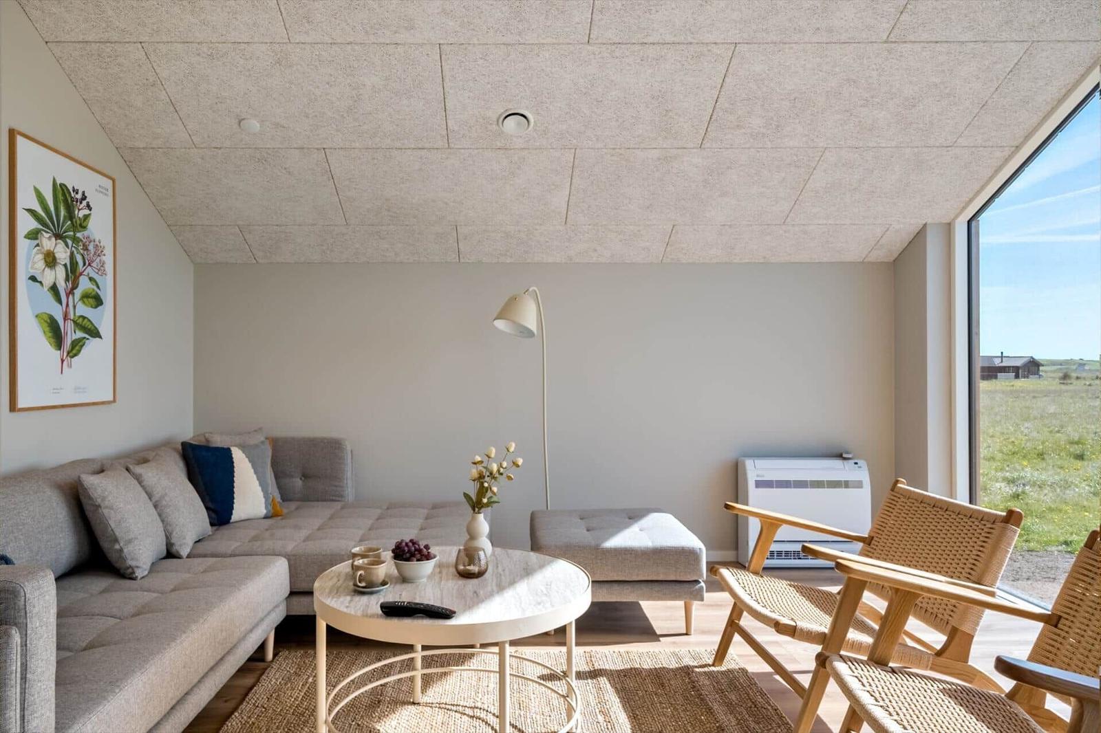 Wohnzimmer mit Sofa, Tisch und Stühlen. Große Fenster und Wandbild.