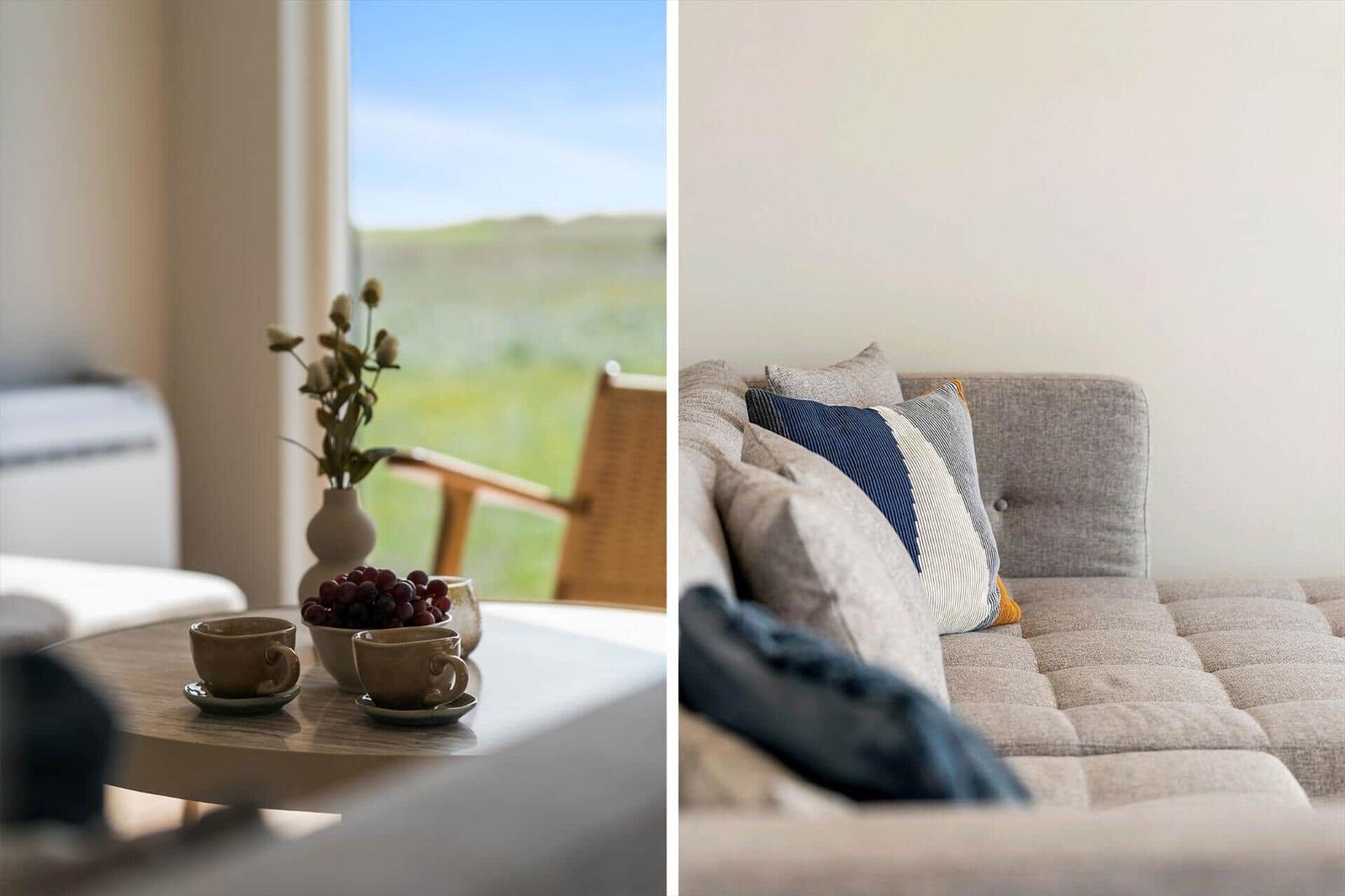 Tisch mit Tassen und Trauben vor Fenster mit Blick auf Grünland. Sofa mit Kissen und gepolstertem Sitzbereich.