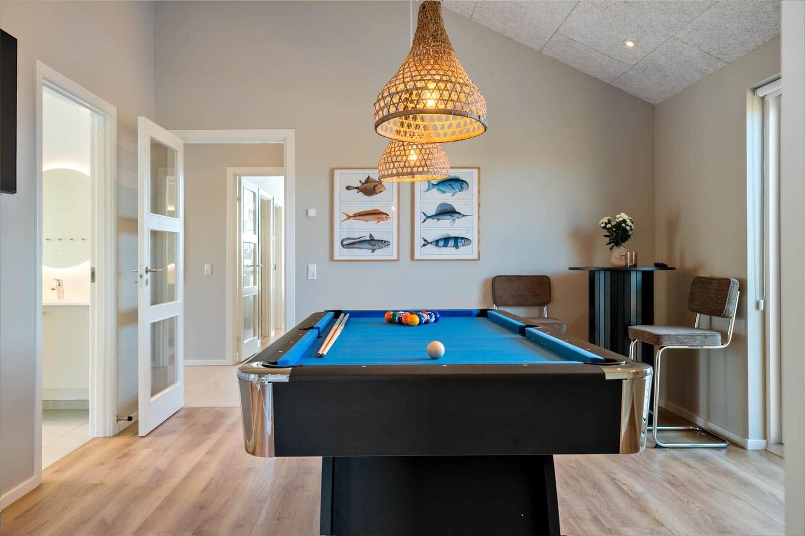 Billardtisch mit blauem Tuch, Wandbilder mit Fischen, hängende Lampe und Sitzgelegenheiten.