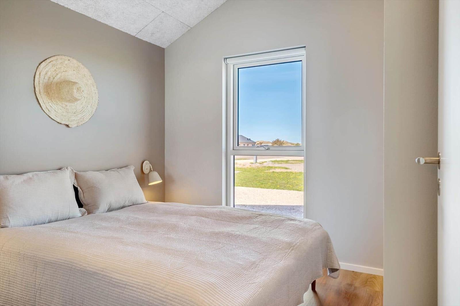 Schlafzimmer mit Bett, Wandlampe und Fensterblick auf Grünfläche.