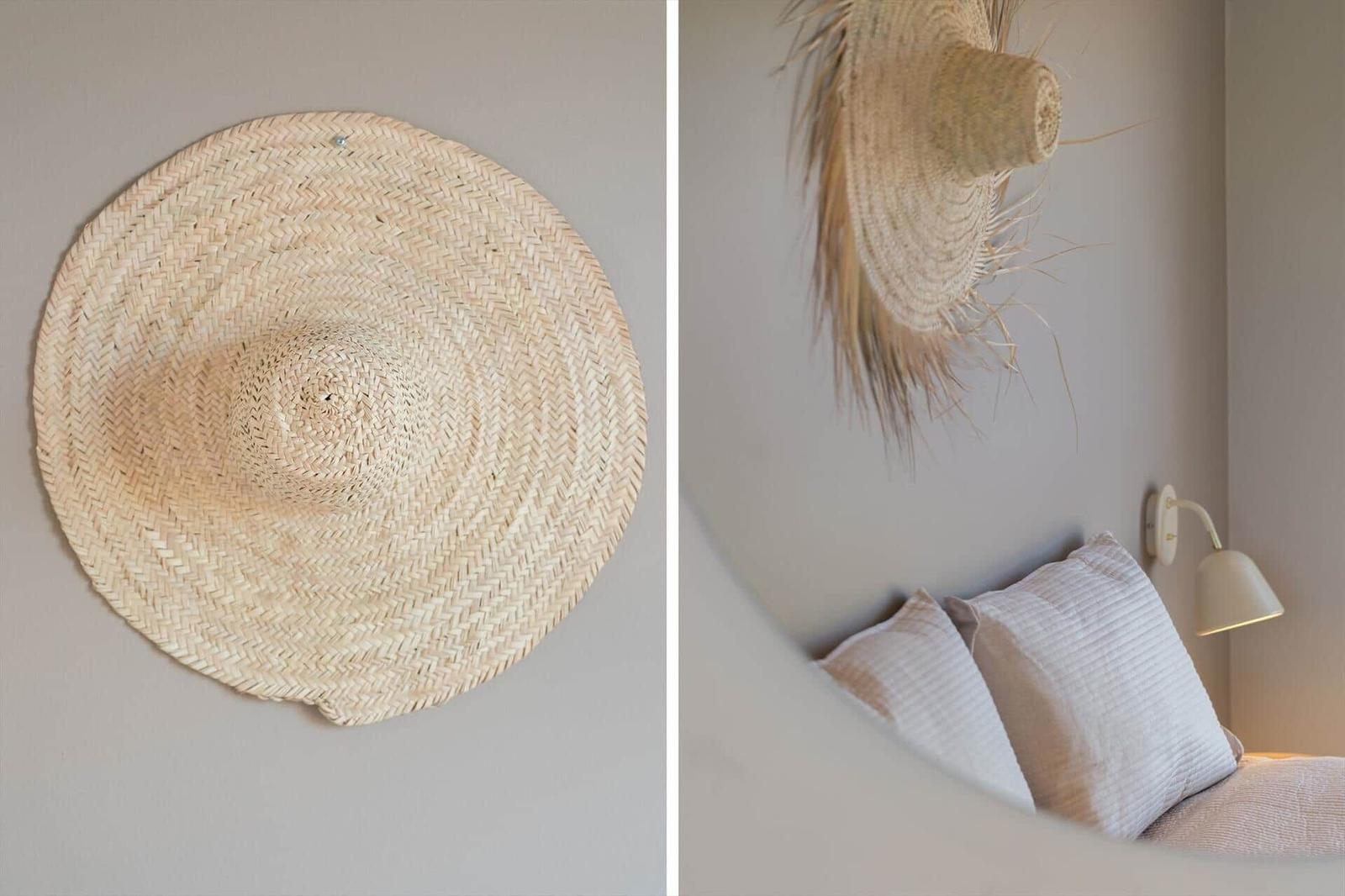 Wandgestellter Strohhut über einem Bett mit Kissen und Wandlampe.