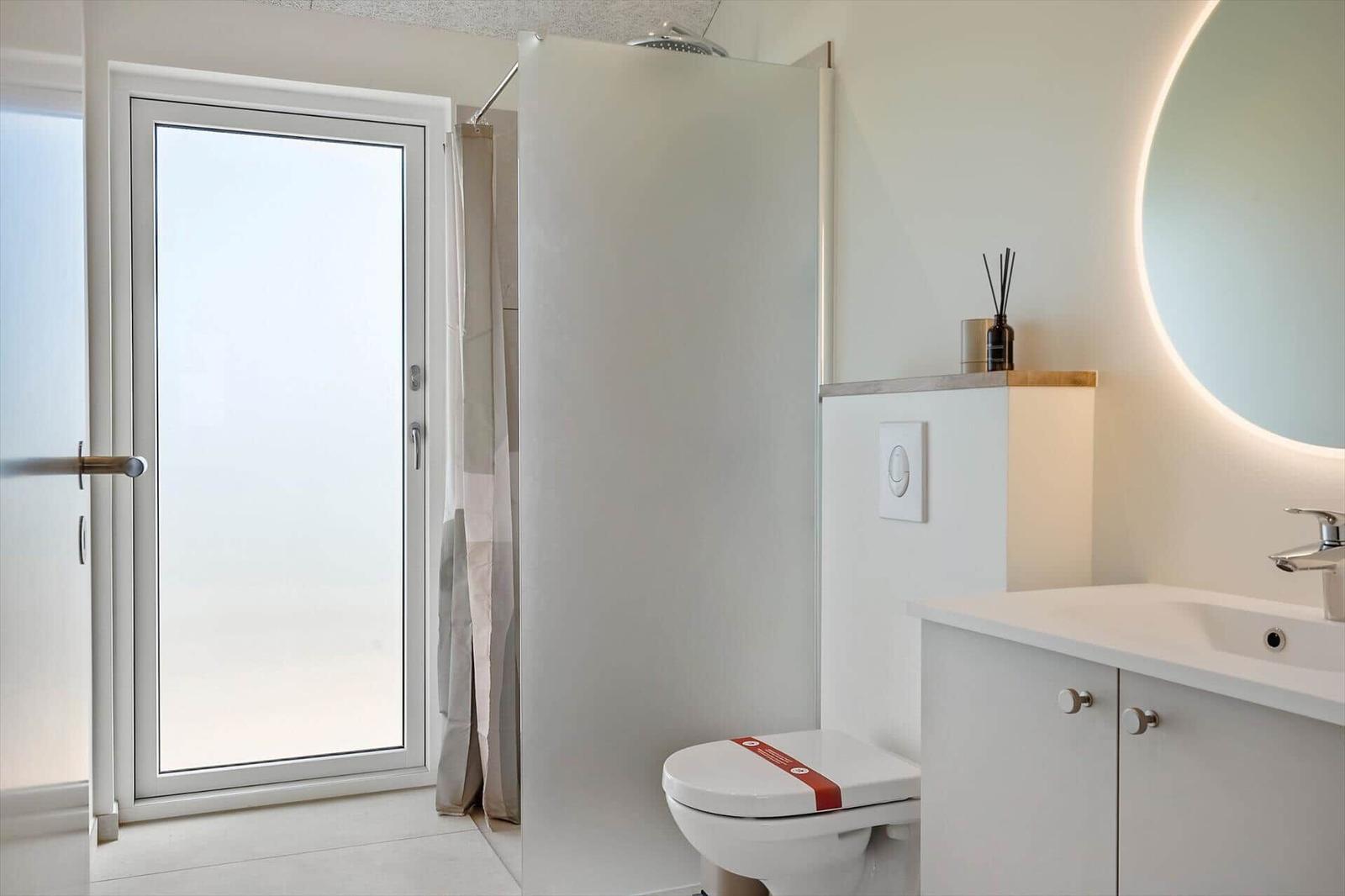 Badezimmer mit Dusche, Toilette und Waschbecken mit runden Spiegel
