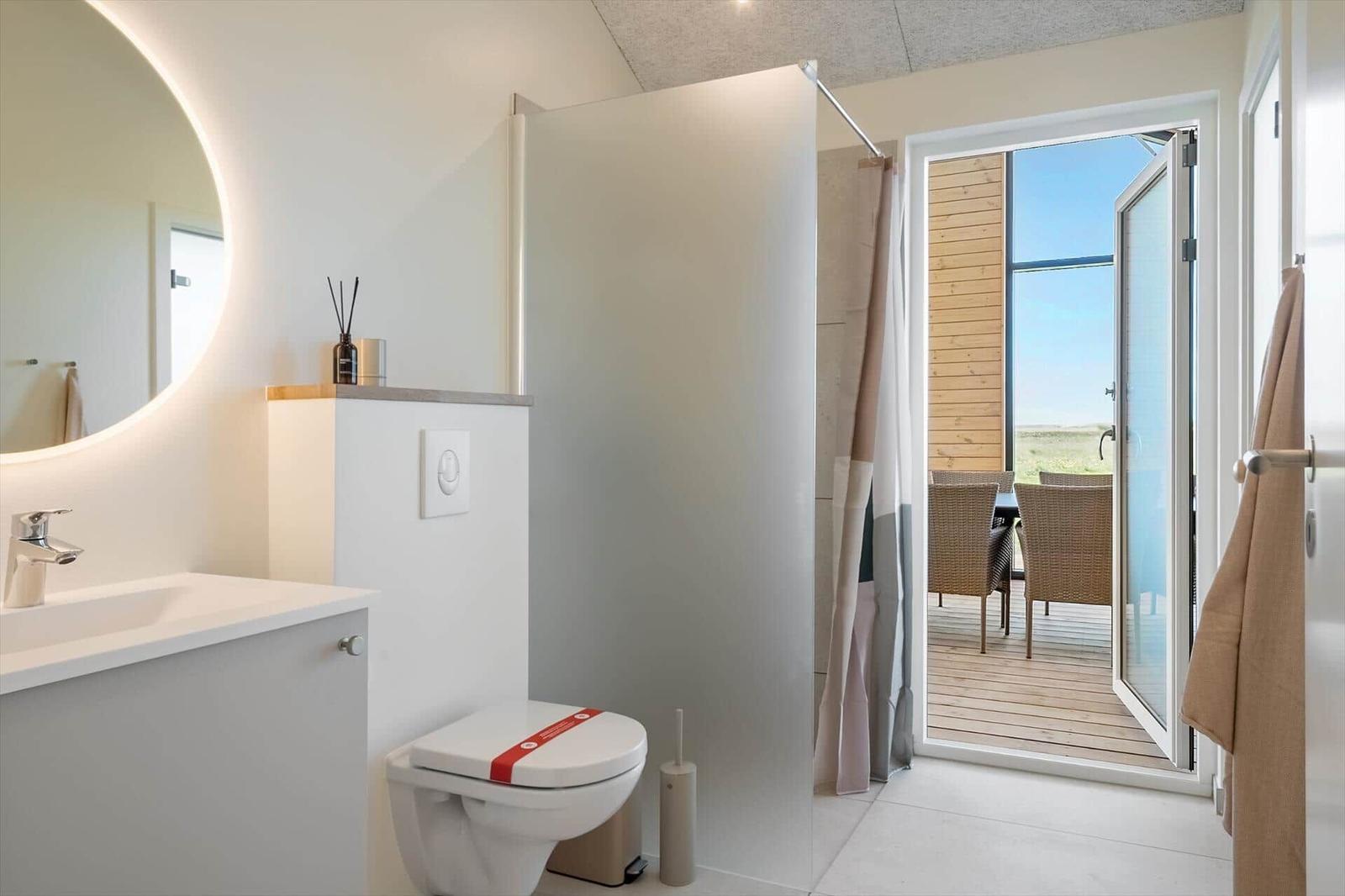Badezimmer mit Waschbecken, Toilette und Dusche. Durchgang zur Terrasse mit Sitzgelegenheit.