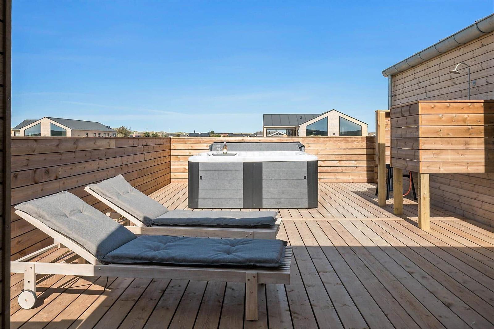 Terrasse mit Whirlpool, Liegestühlen und Holzumrandung. Blick auf moderne Häuser im Hintergrund.