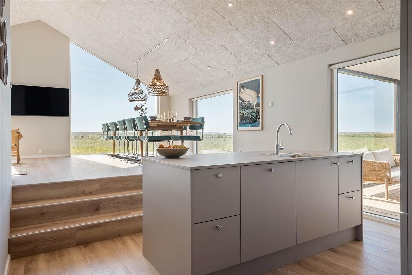 Küche mit Insel, Essbereich und großzügigen Fenstern mit Blick auf Landschaft.