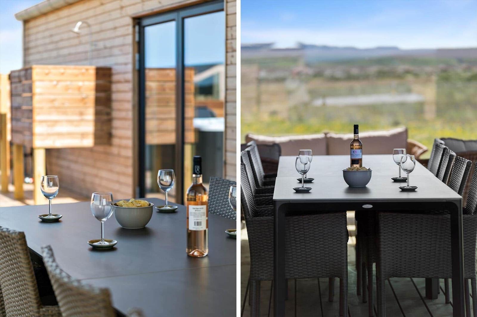 Terrasse mit Tisch, Stühlen, Wein und Snacks. Blick auf Landschaft.