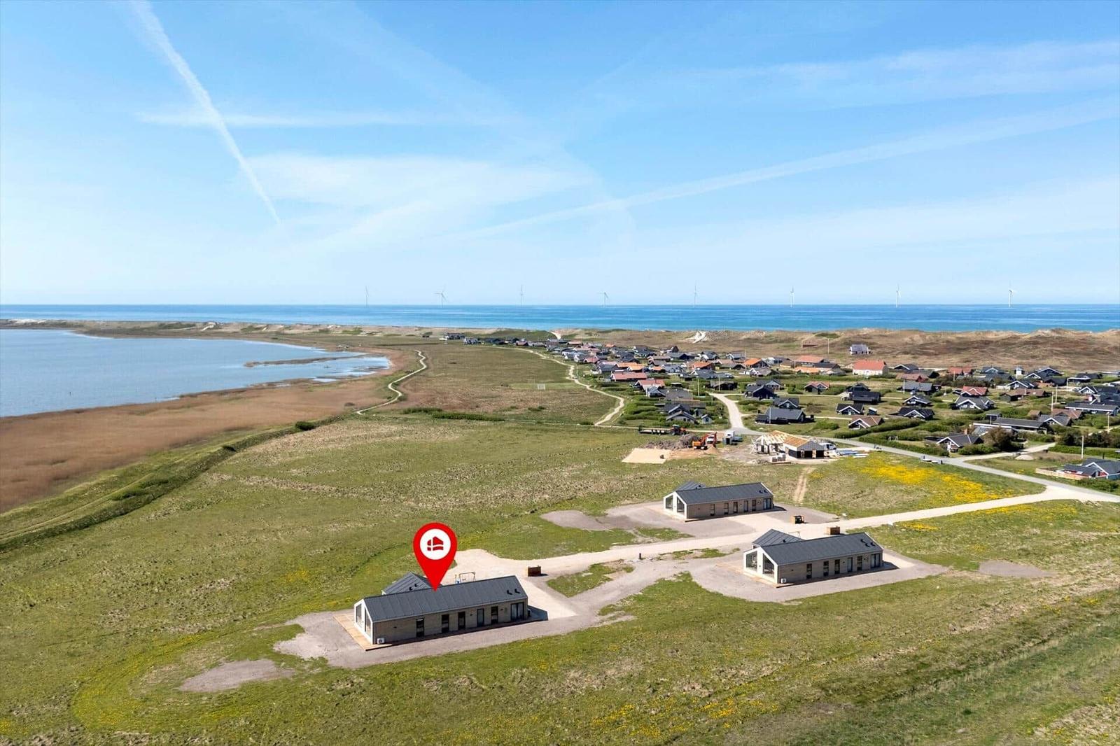 Modernes Ferienhaus auf grünem Gelände mit Blick auf Meer und Windkraftanlagen.