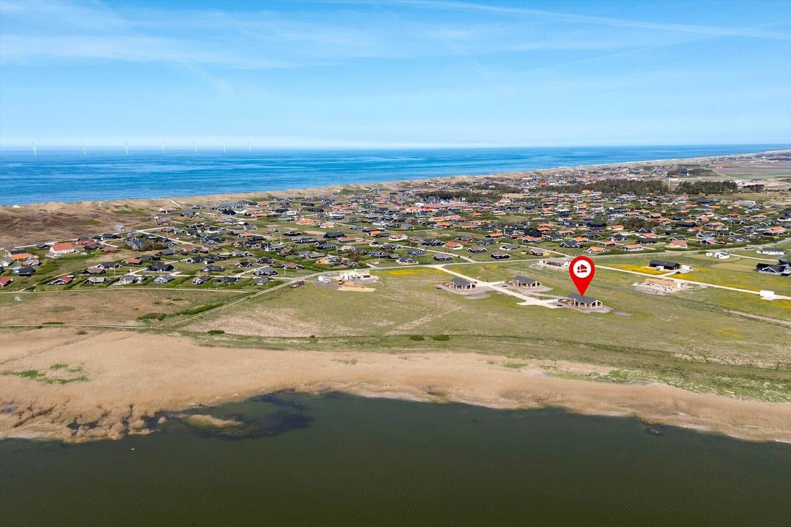 Aerial view of a coastal village with houses, a river, and wind turbines on the horizon.