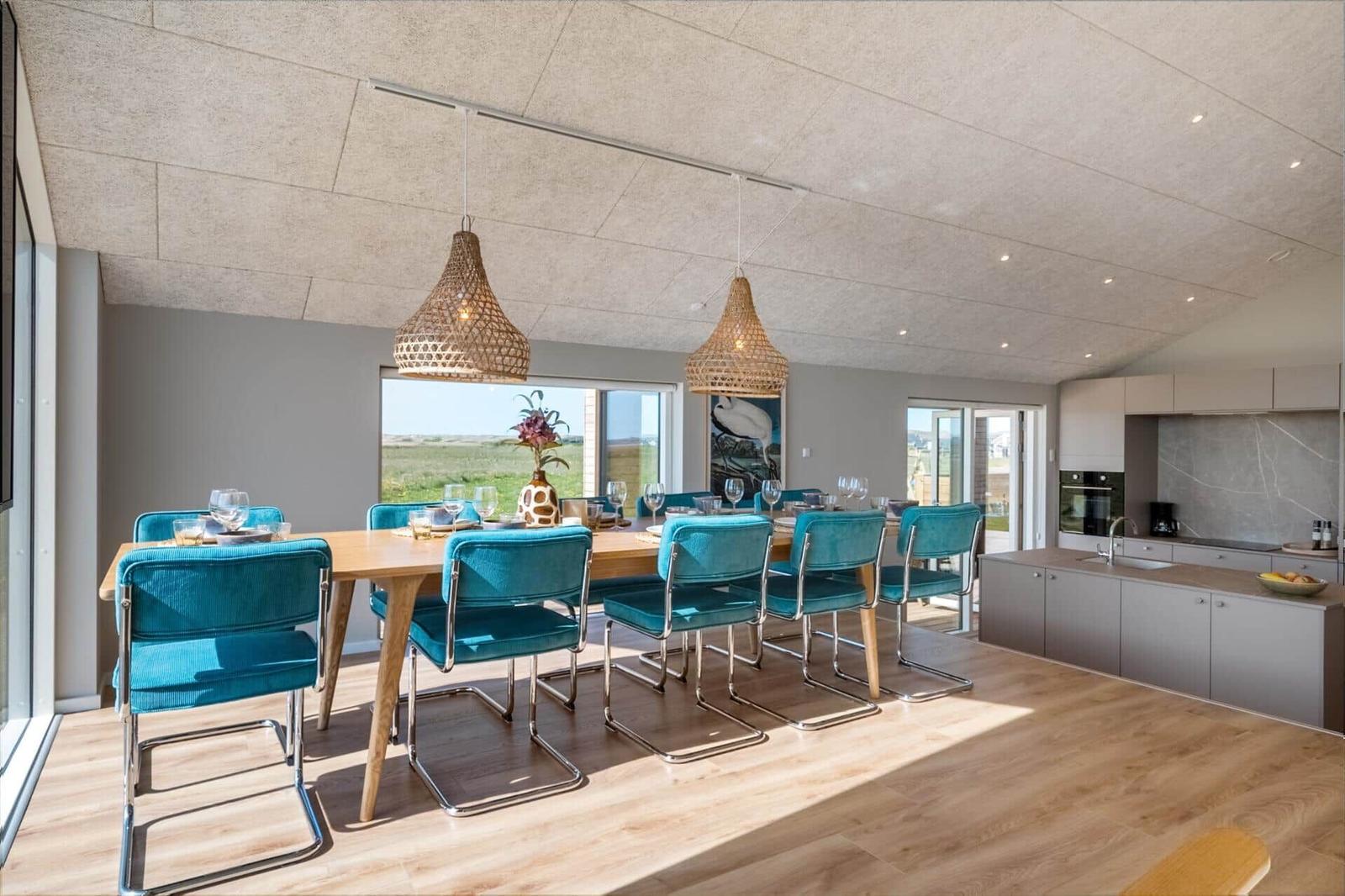 Essbereich mit blauen Stühlen und Holztisch. Küche mit grauen Schränken. Fenster mit Blick auf Grasland.