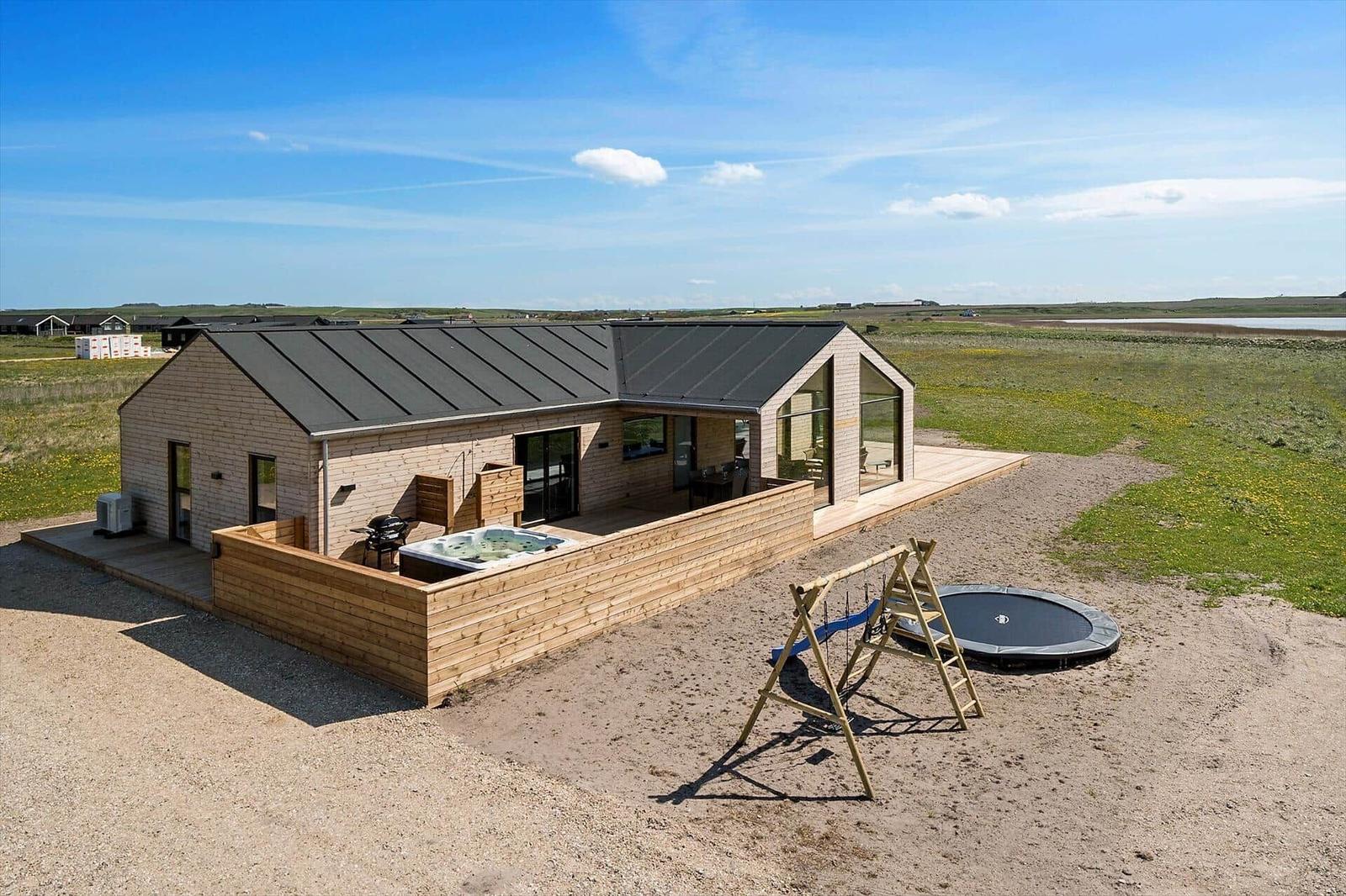 Moderne Villa mit Whirlpool, Trampolin und Spielplatz auf sandigem Grundstück.