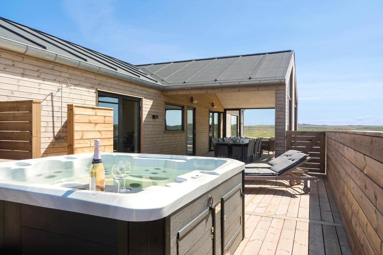 Hochwertige Außenterrasse mit Whirlpool, Liegen und Blick auf die Landschaft.
