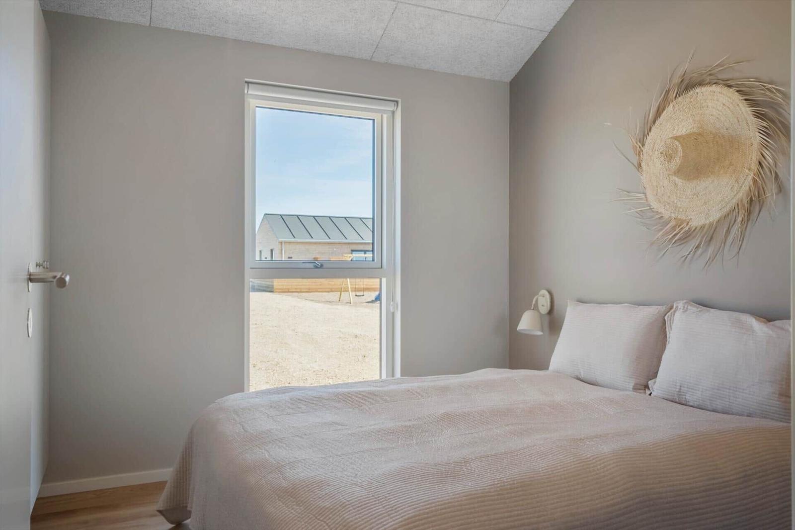 Schlafzimmer mit Bett, Wandlampe und Fensterblick auf Außenbereich