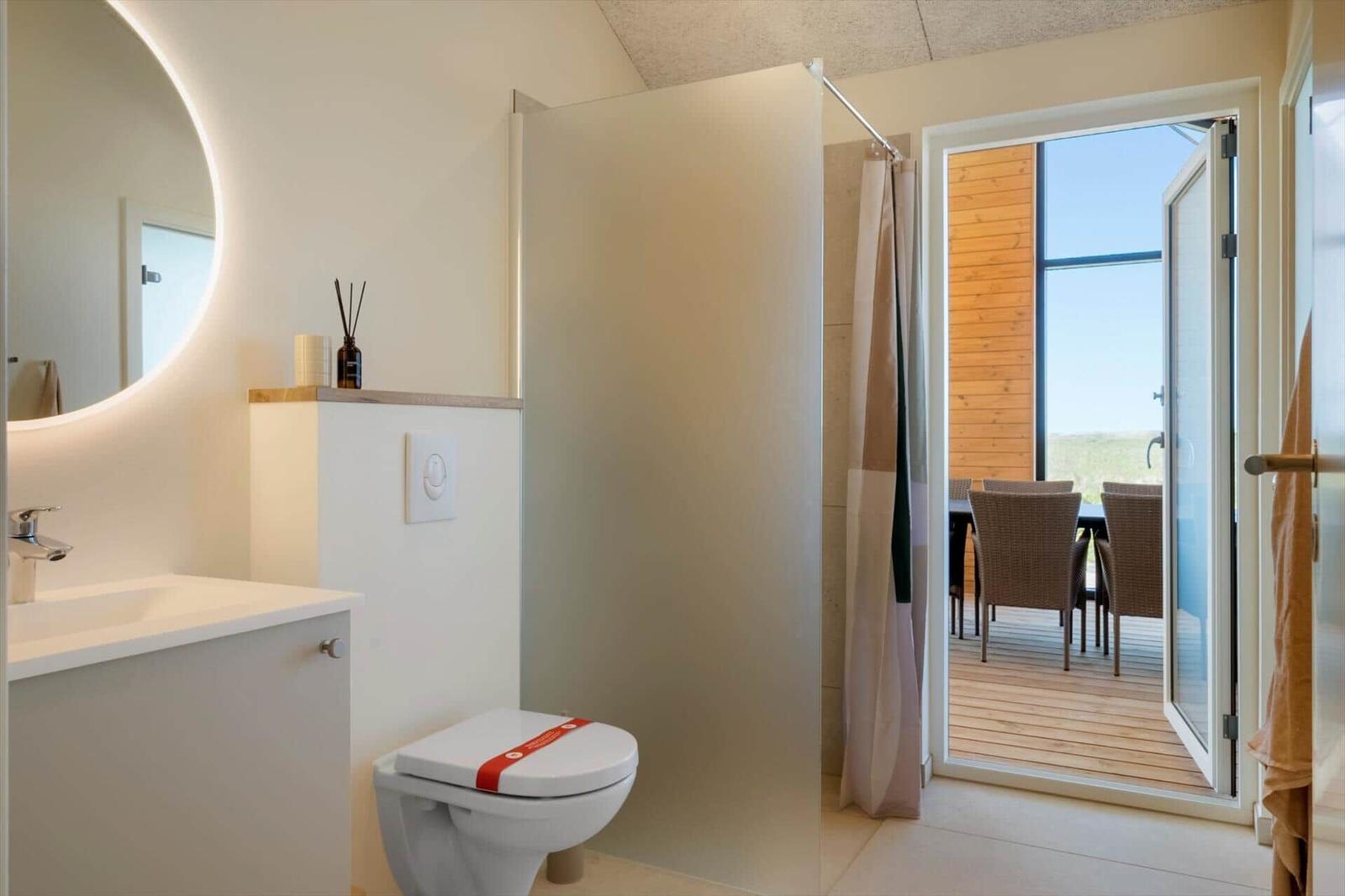 Badezimmer mit Toilette, Waschbecken und Dusche. Durchgang zur Terrasse mit Tisch und Stühlen.