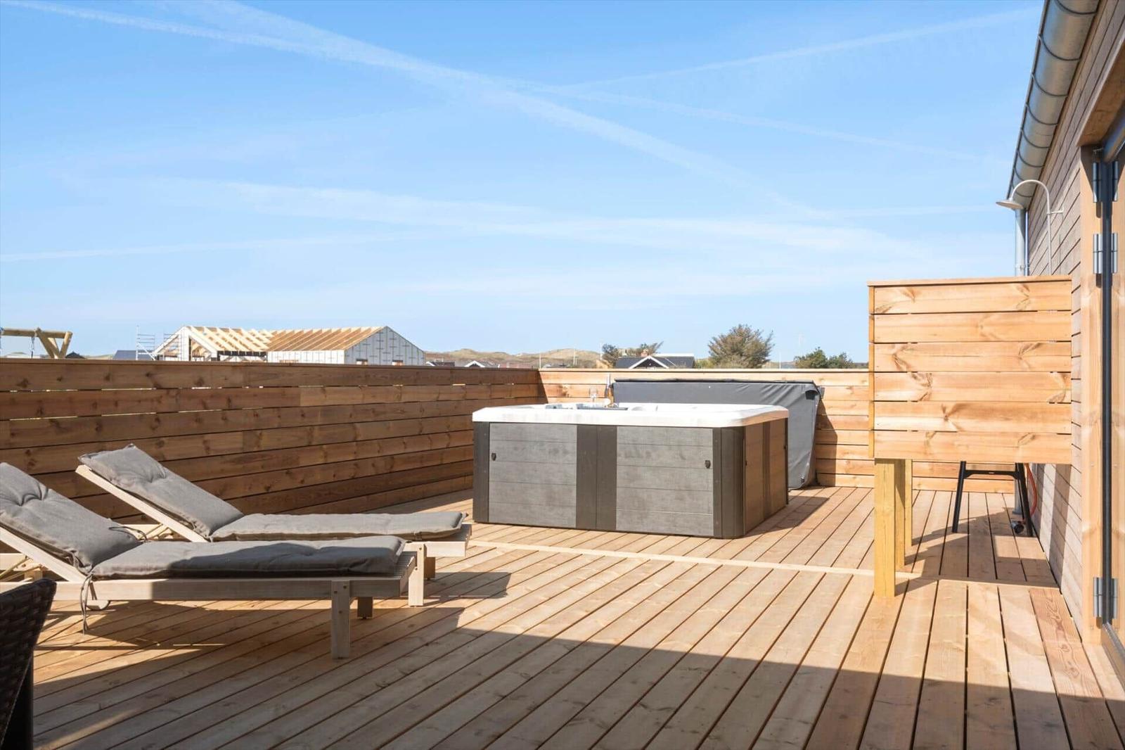 Terrasse mit Whirlpool, Liegestühlen und Holzgeländer unter blauem Himmel.