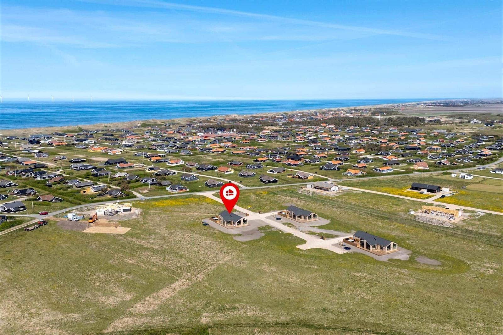 Luftbild einer Ferienanlage mit mehreren Häusern, Grünflächen und Blick auf das Meer.