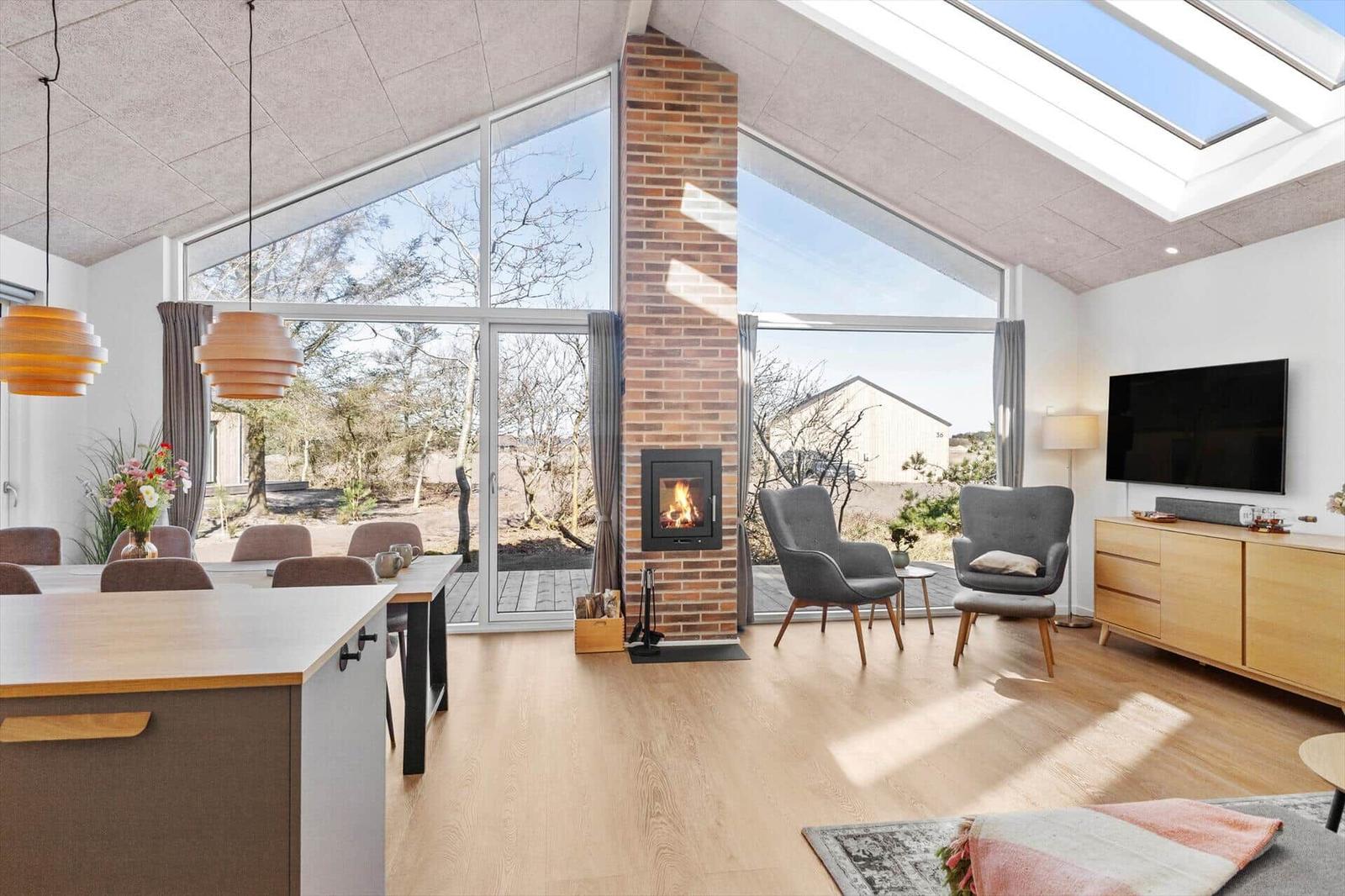 Wohn- und Essbereich mit Kamin, großen Fenstern und Holzboden.