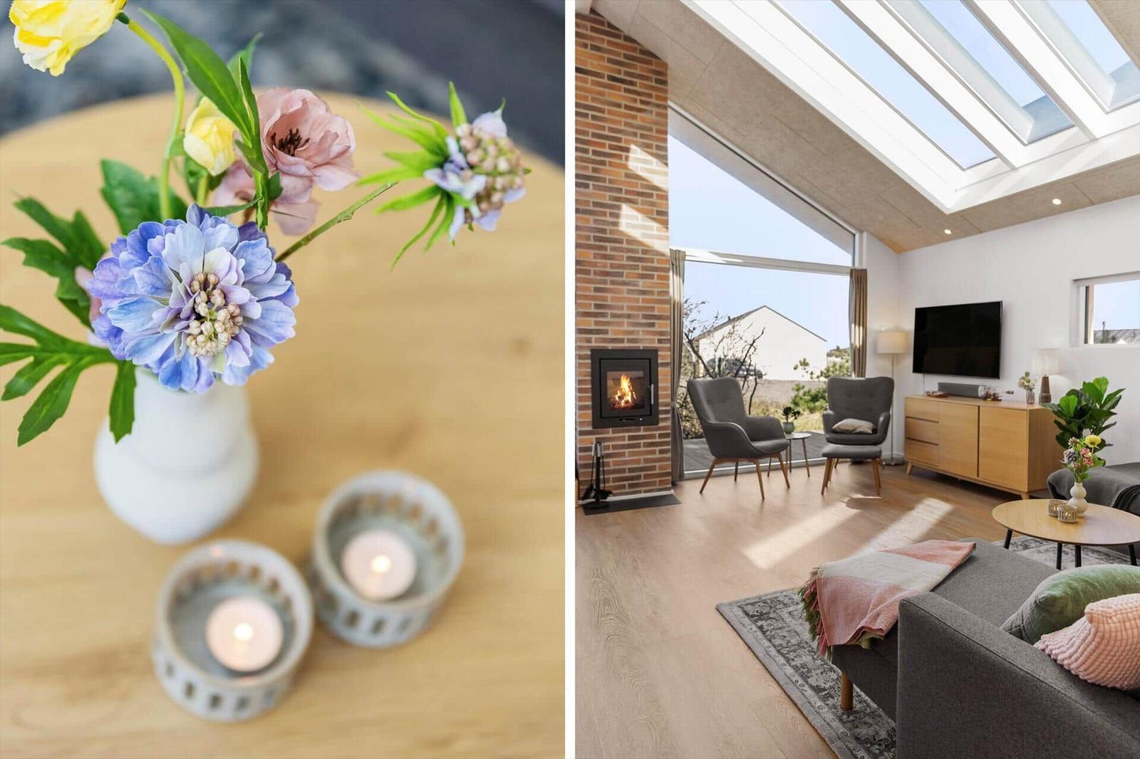 Ein Wohnzimmer mit Kamin, großen Fenstern und Dachfenstern. Blumen und Kerzen auf einem Tisch.