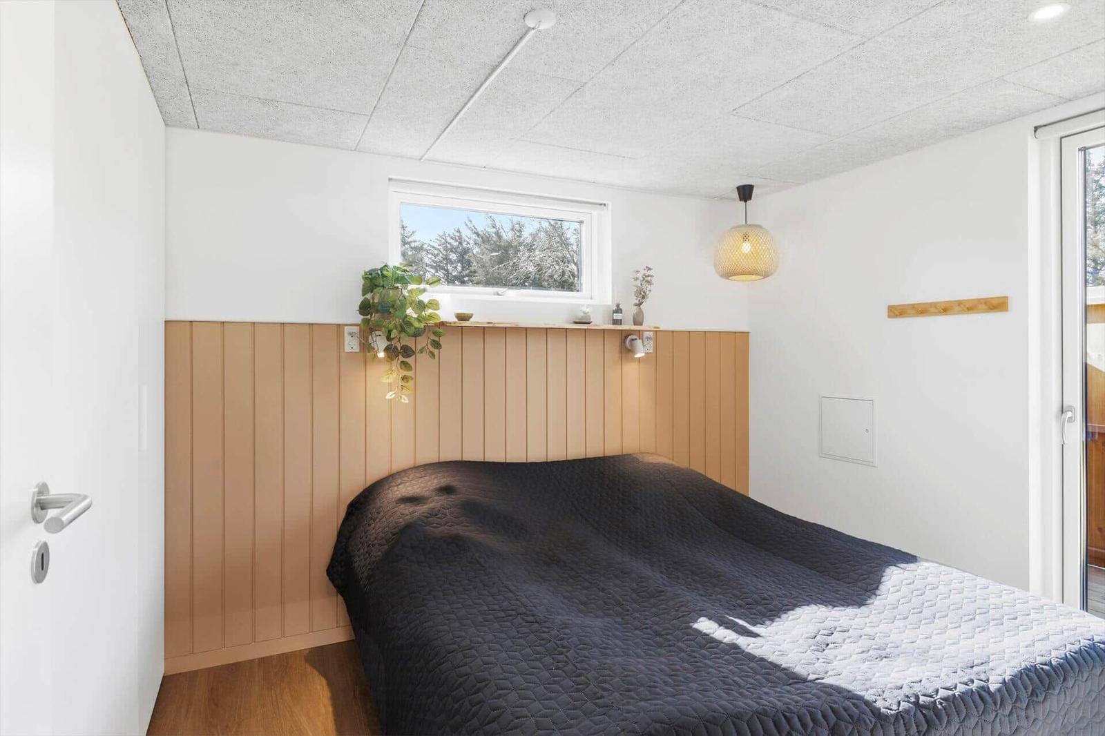 Schlafzimmer mit Bett, Holzwand und Fenster. Decke mit Lampe und Pflanze.