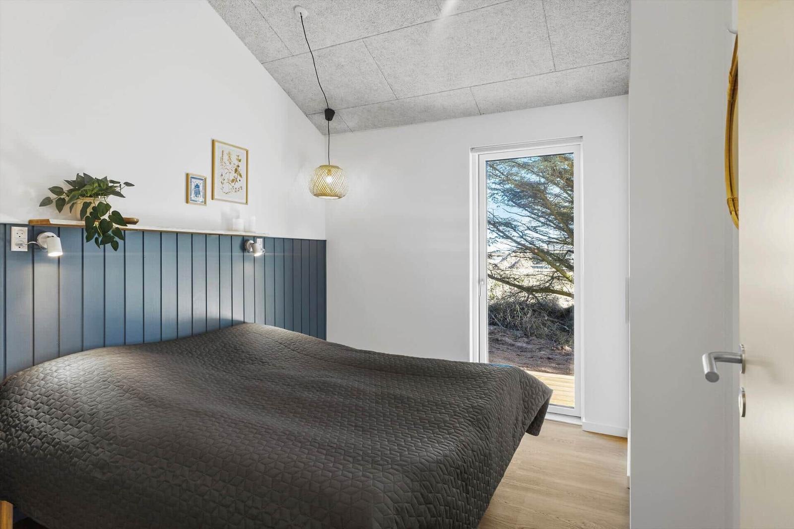 Schlafzimmer mit Bett, Fenster und Wandverkleidung.