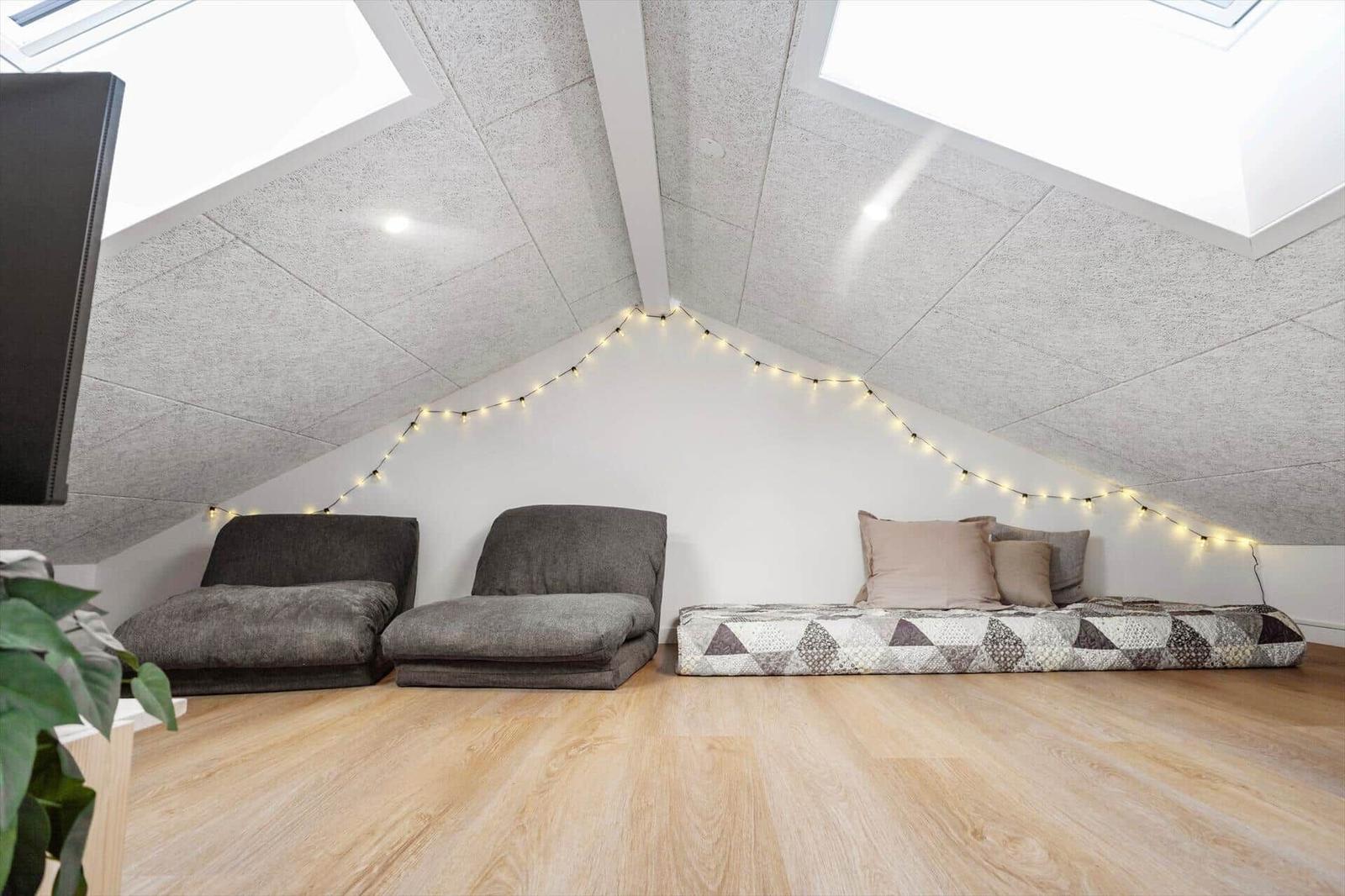 Zimmer mit Dachschrägen, zwei Sitzkissen und Matratze mit Kissen.
