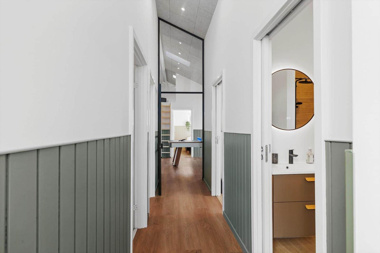 Flur mit Holzboden und grauer Paneelwand, Blick in Schlafzimmer und Badezimmer.