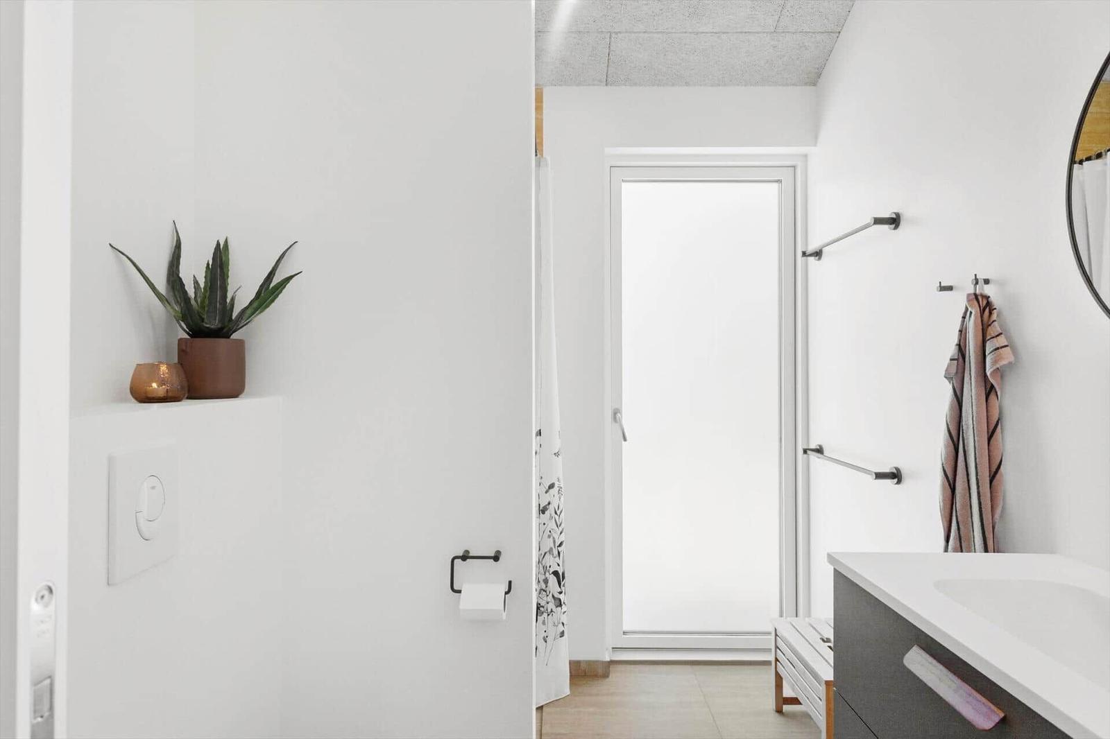 Badezimmer mit Toilette, Waschtisch und Dusche. Auf der Wand steht eine Pflanze.
