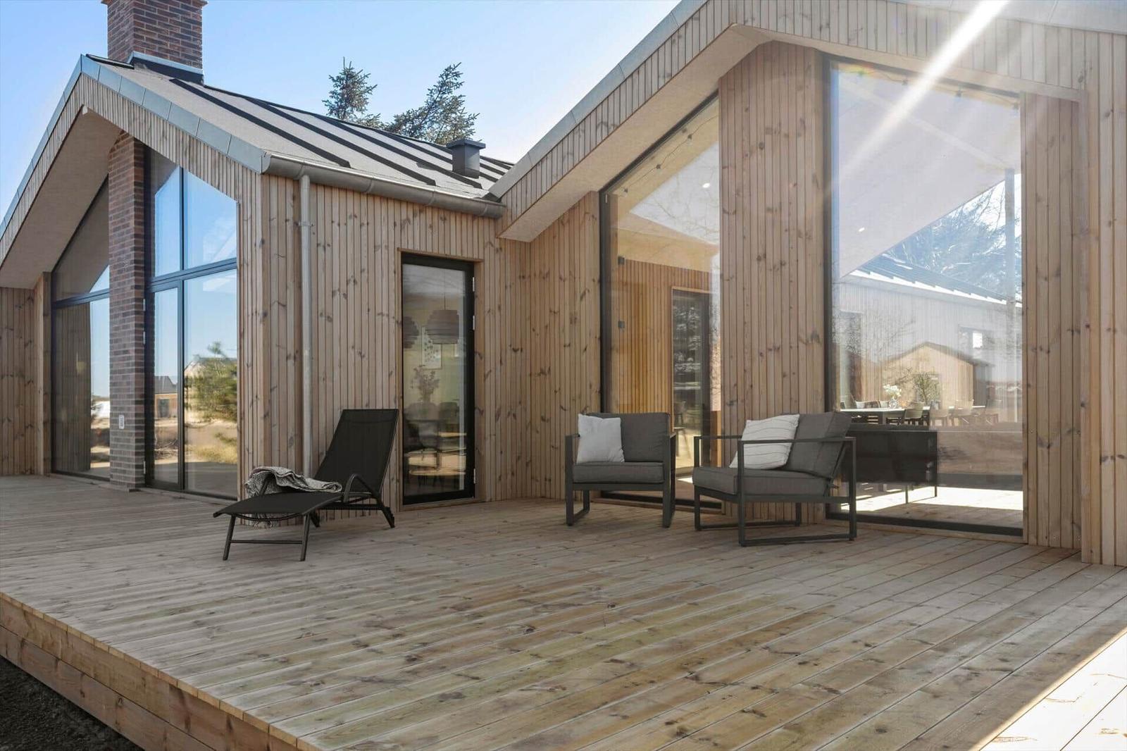 Terrasse mit Sitzgelegenheiten und Holzwandhaus mit großzügigen Fenstern.