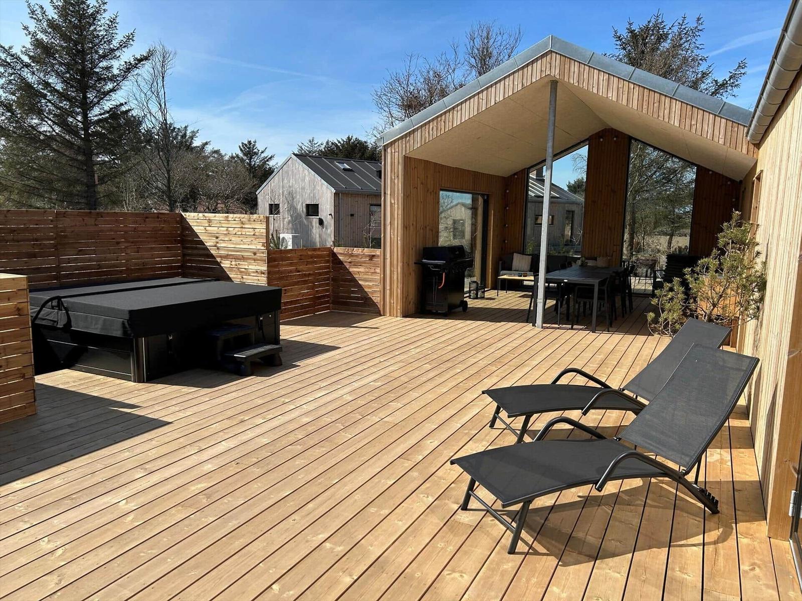 Terrasse mit Liegestühlen, Grill und Whirlpool. Holzdeck und Sicht auf Wald.