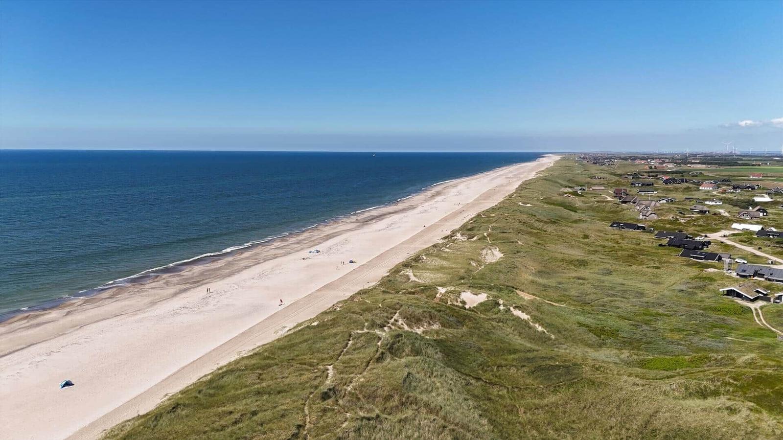 Strand mit Dünen und Häusern am Meer unter blauem Himmel