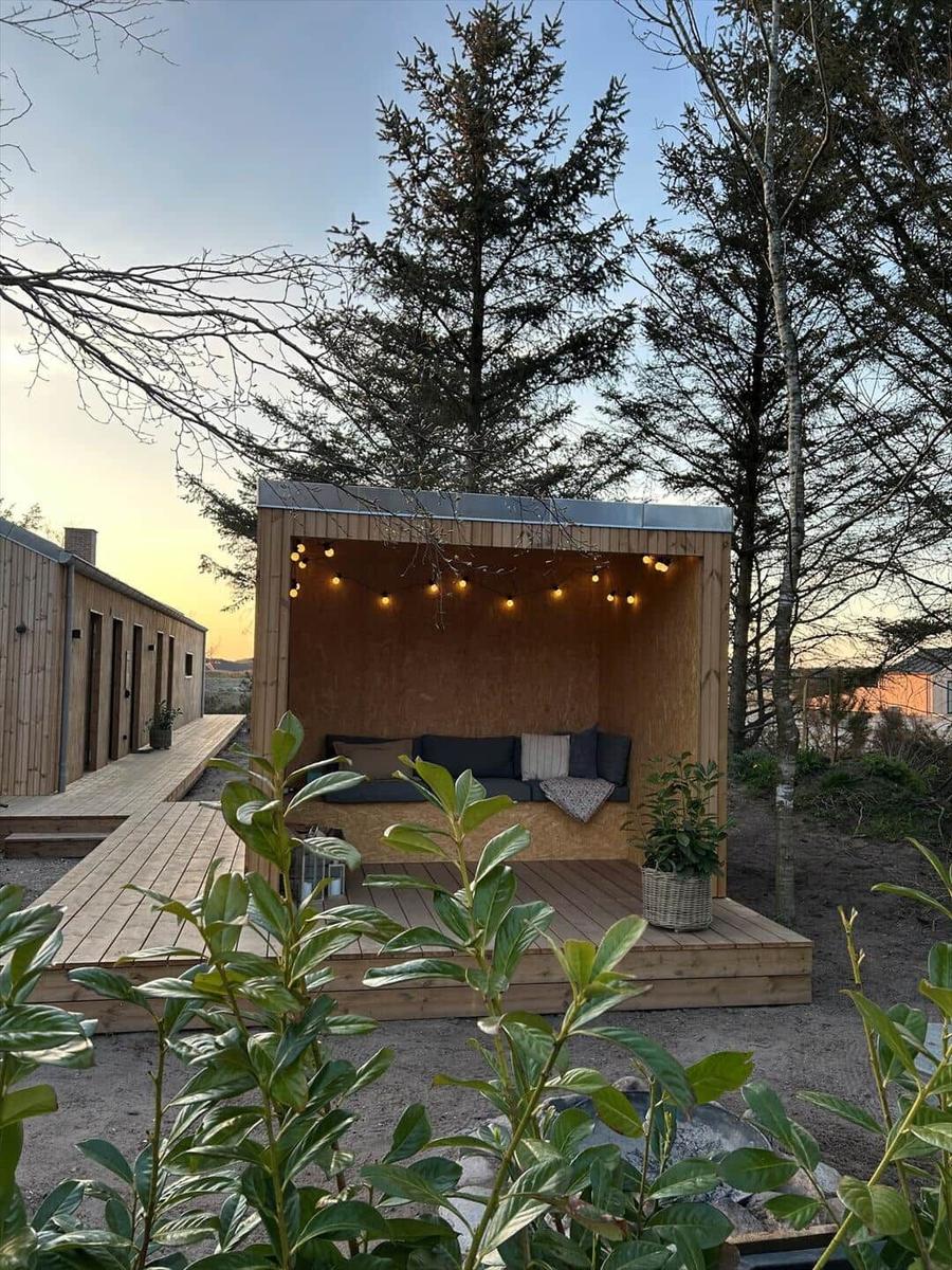 Holzüberdachter Sitzbereich mit Sofa, Beleuchtung und Pflanze im Freien.