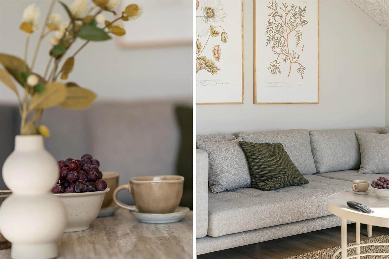 Grauer Sofa mit Kissen, Tisch mit Tasse und Trauben, Wand mit Pflanzenbildern