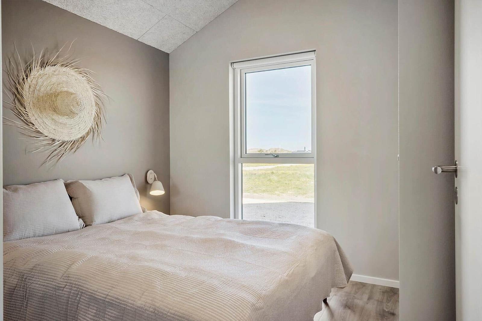 Schlafzimmer mit Bett, Wanddekoration und Fensterblick auf Grünfläche