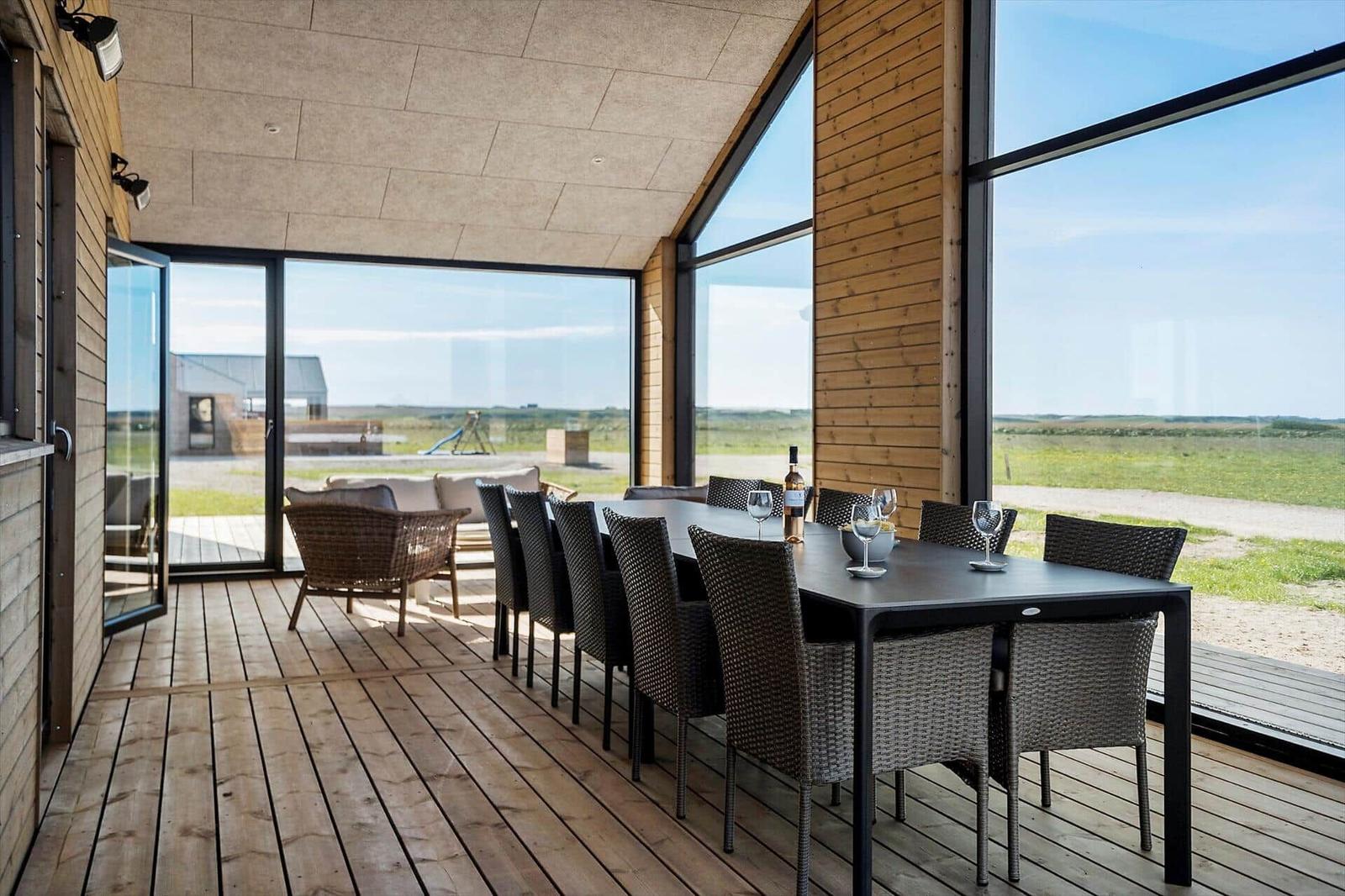 Terrasse mit Esstisch und Stühlen. Große Fenster bieten Blick auf Felder.