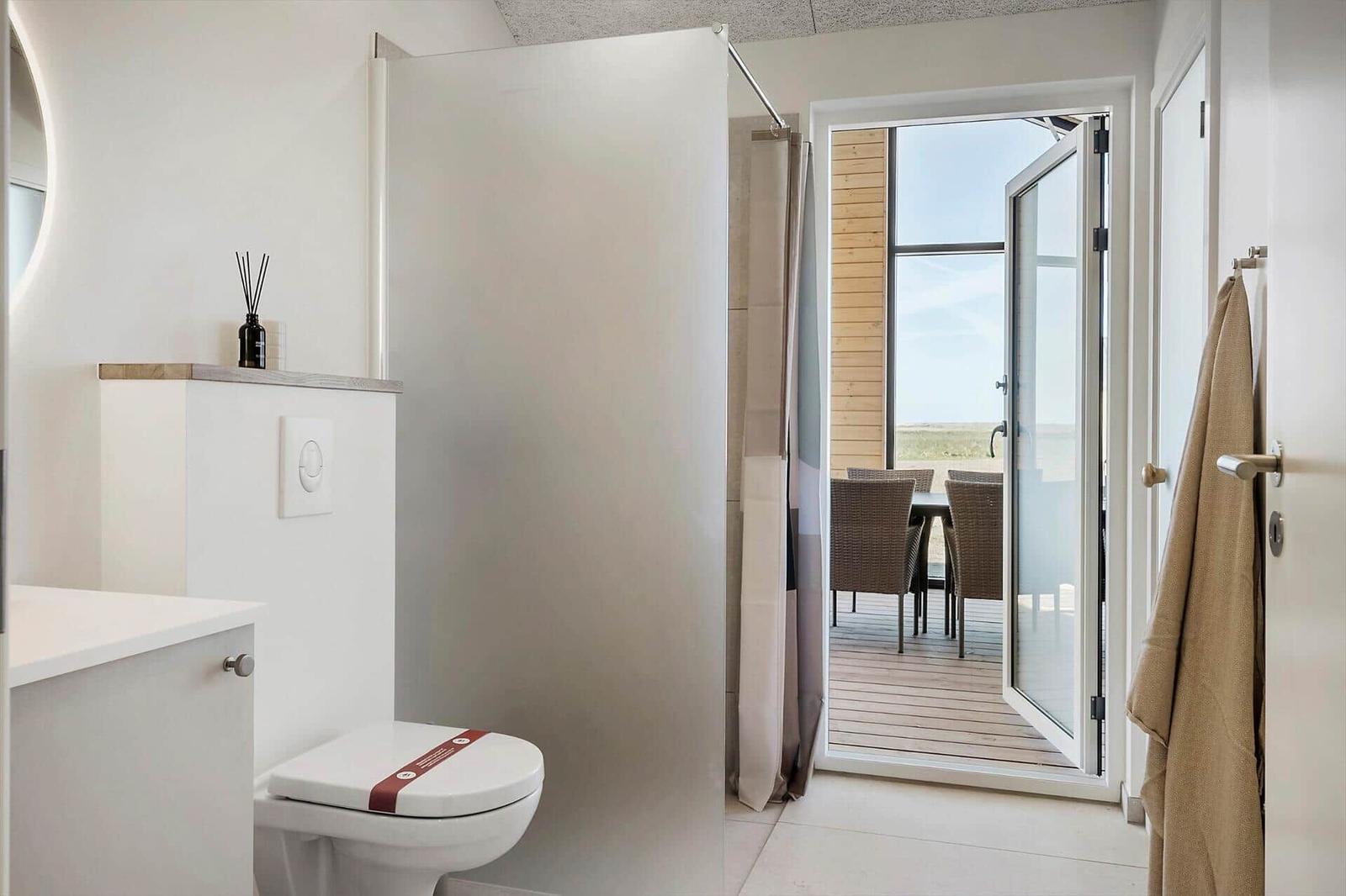 Badezimmer mit Toilette und Dusche. Durchgehendes Fenster zum Balkon mit Sitzgelegenheiten.