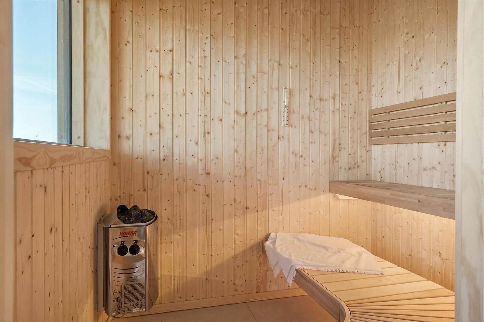 Sauna mit Holzwand, Bank und Heizgerät. Fenster zeigt Himmel.
