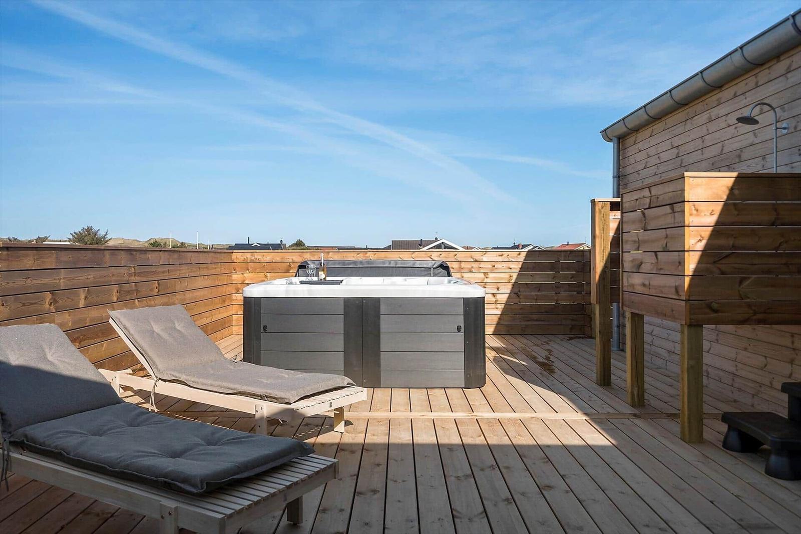 Terrasse mit Whirlpool, Sonnenliegen und Holzwand. Dachüberdachung und Dusche vorhanden.