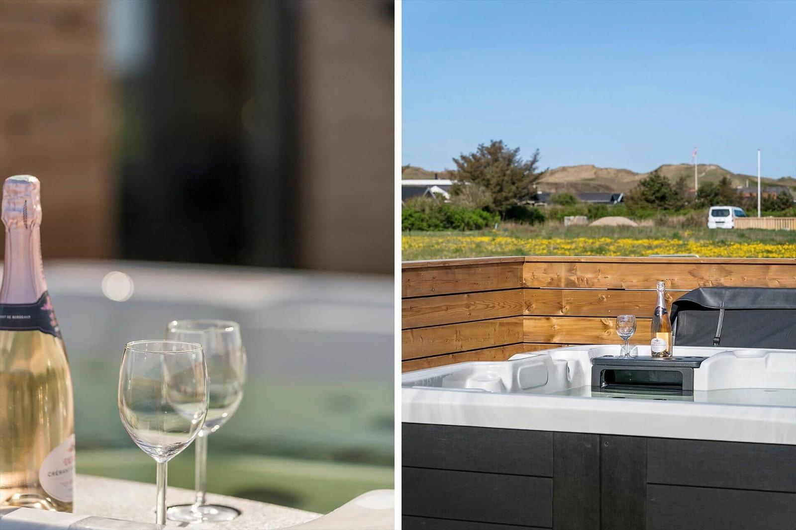 Whirlpool mit Sekt und Gläsern auf Terrasse mit Blick auf Wiese und Hügel.