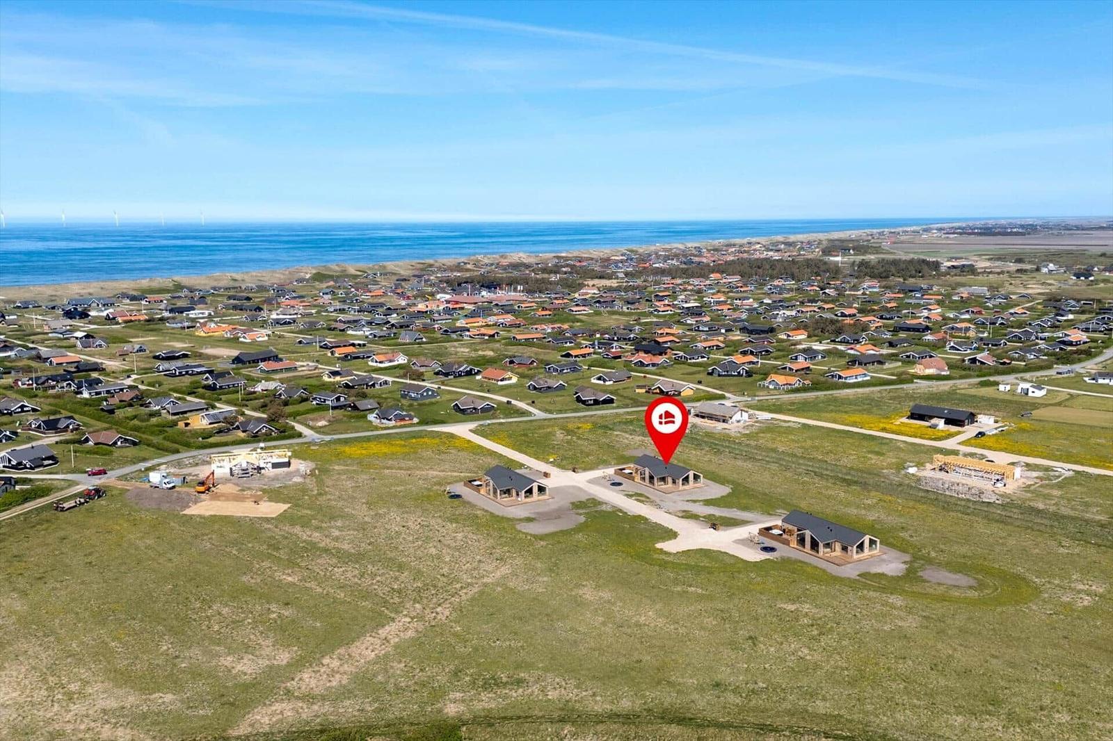 Aerial view of a coastal village with modern houses and a red location marker.