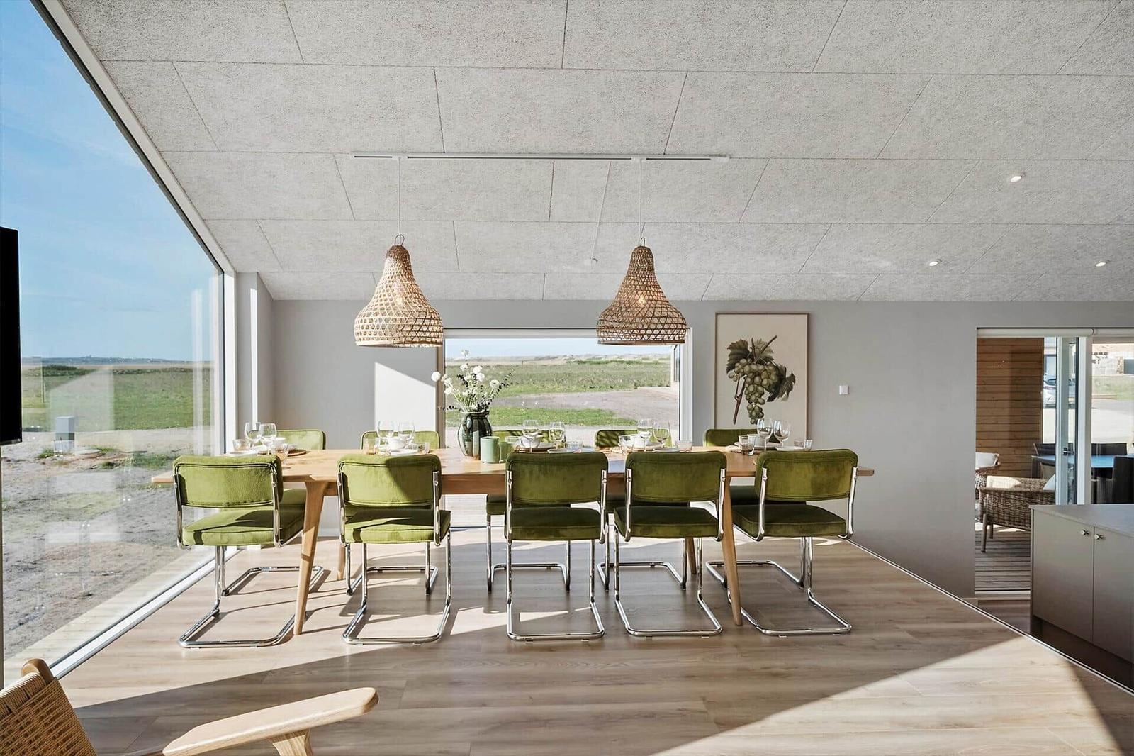 Esszimmer mit grünen Stühlen, Holztisch und großen Fenstern mit Blick auf Landschaft.