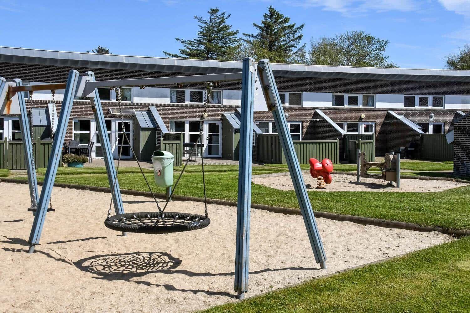 Kinderspielplatz mit Schaukel und Sandkasten vor Ferienwohnungen.