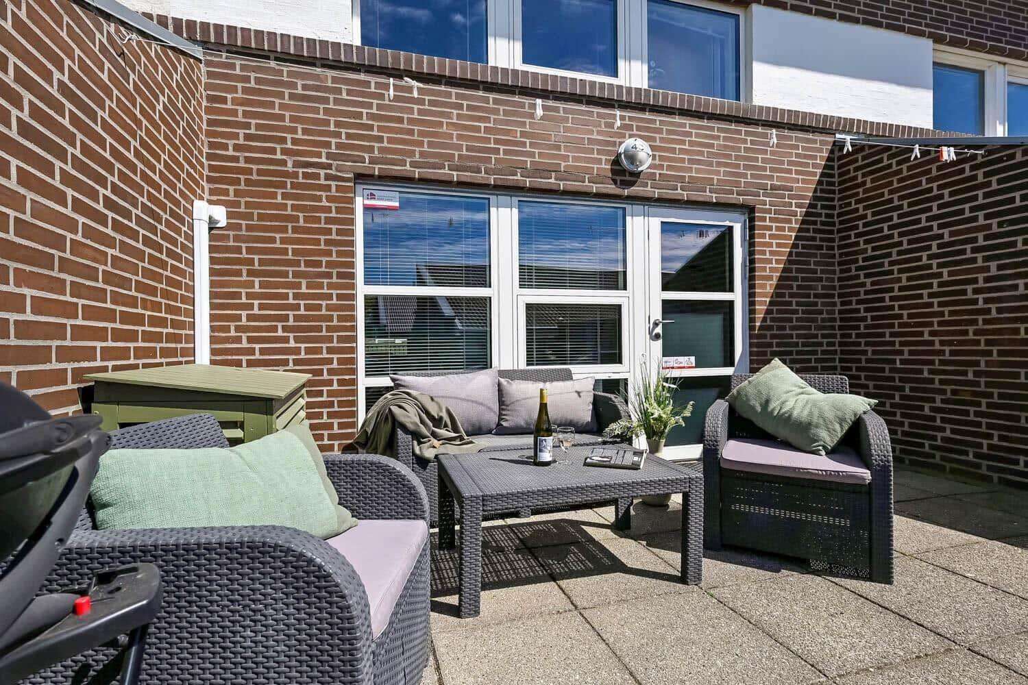 Terrasse mit Sitzgruppe, Tisch und Grill. Hintergrund: Backsteinmauer und Fenster.