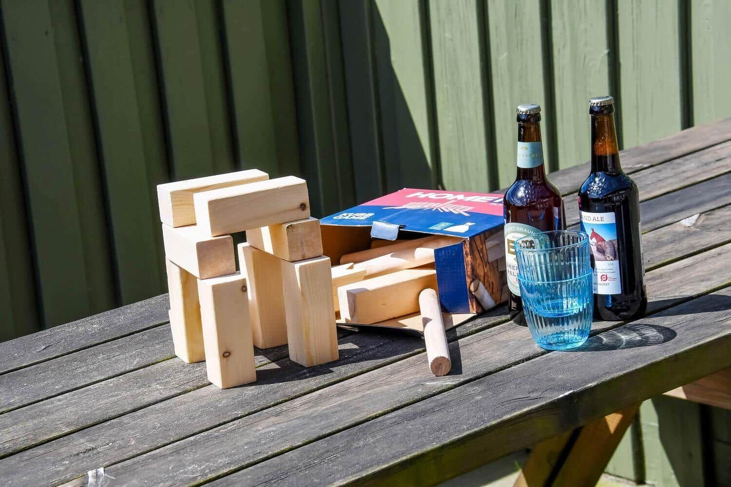 Holzbausteine, zwei Bierflaschen und ein Glas auf einer Holzbank im Freien.