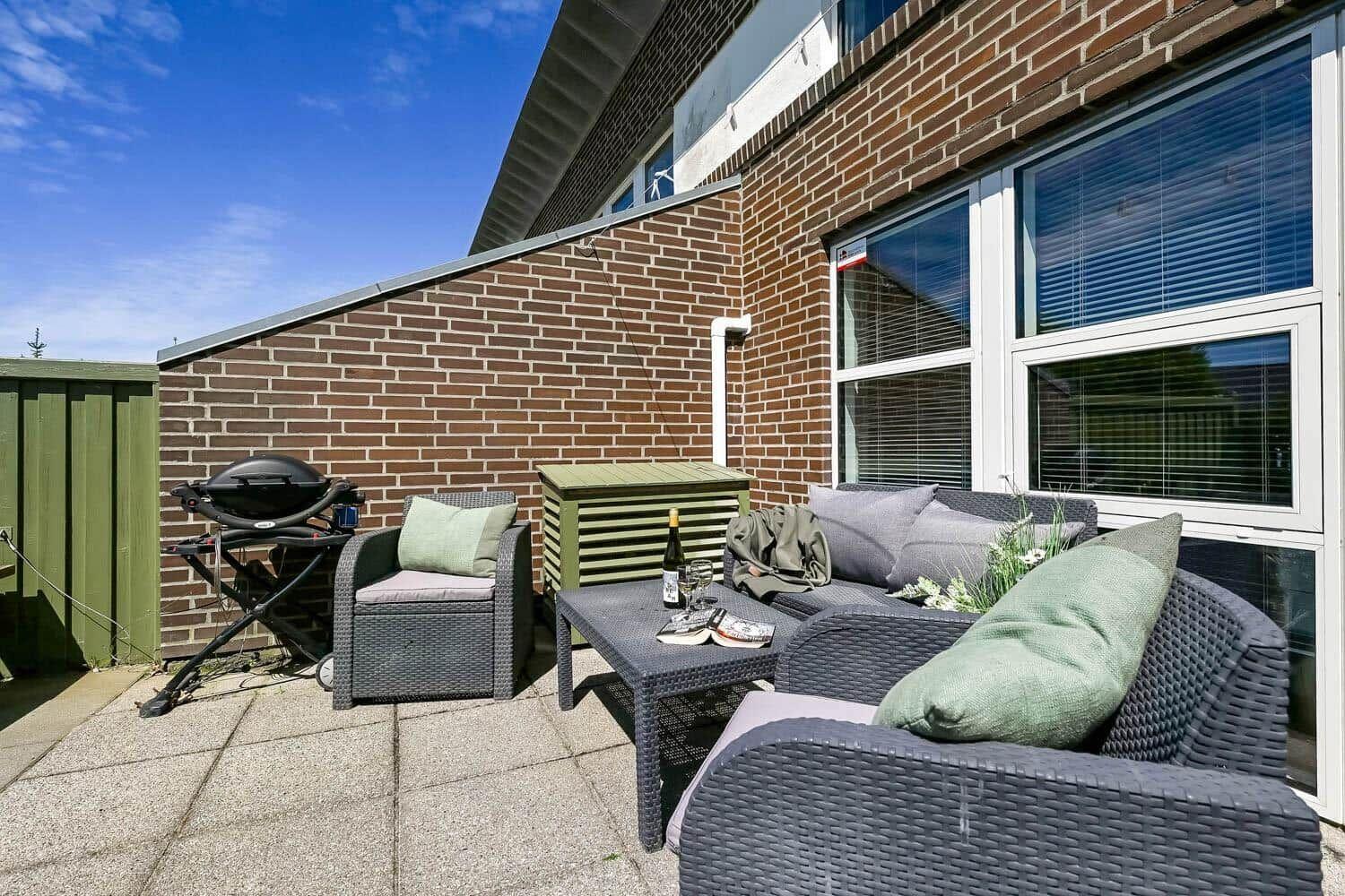Terrasse mit Sitzgruppe, Grill und Fenstern an Backsteinwand.