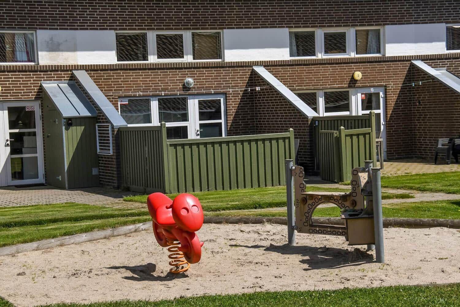 Spielplatz mit rotem Schaukelgerät und Sandkasten vor Wohnhaus