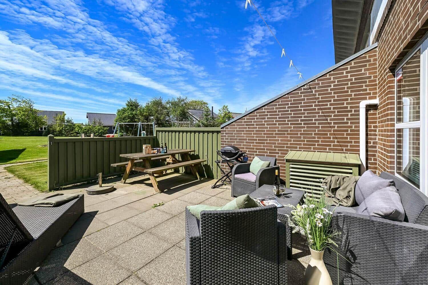 Terrasse mit Sitzgruppe, Grill und Picknicktisch. Hinterhof mit grünem Zaun und Garten.