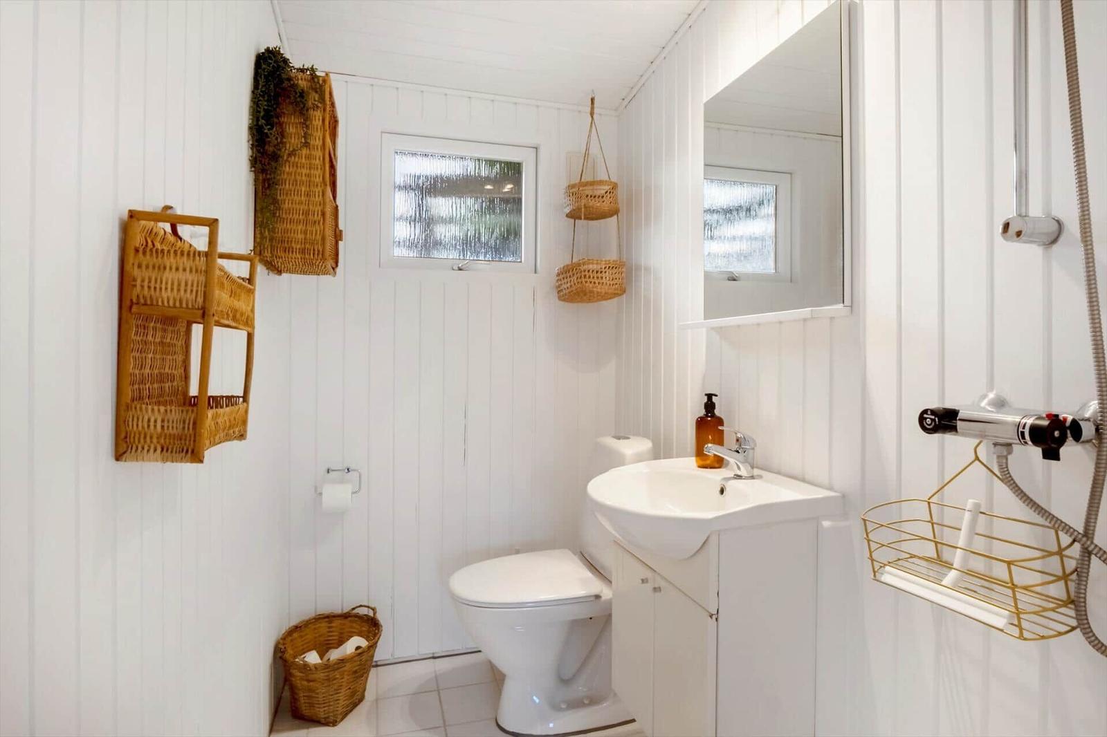 Badezimmer mit Toilette, Waschbecken und Dusche. Wandverkleidung weiß, Körbe aus Rattan.