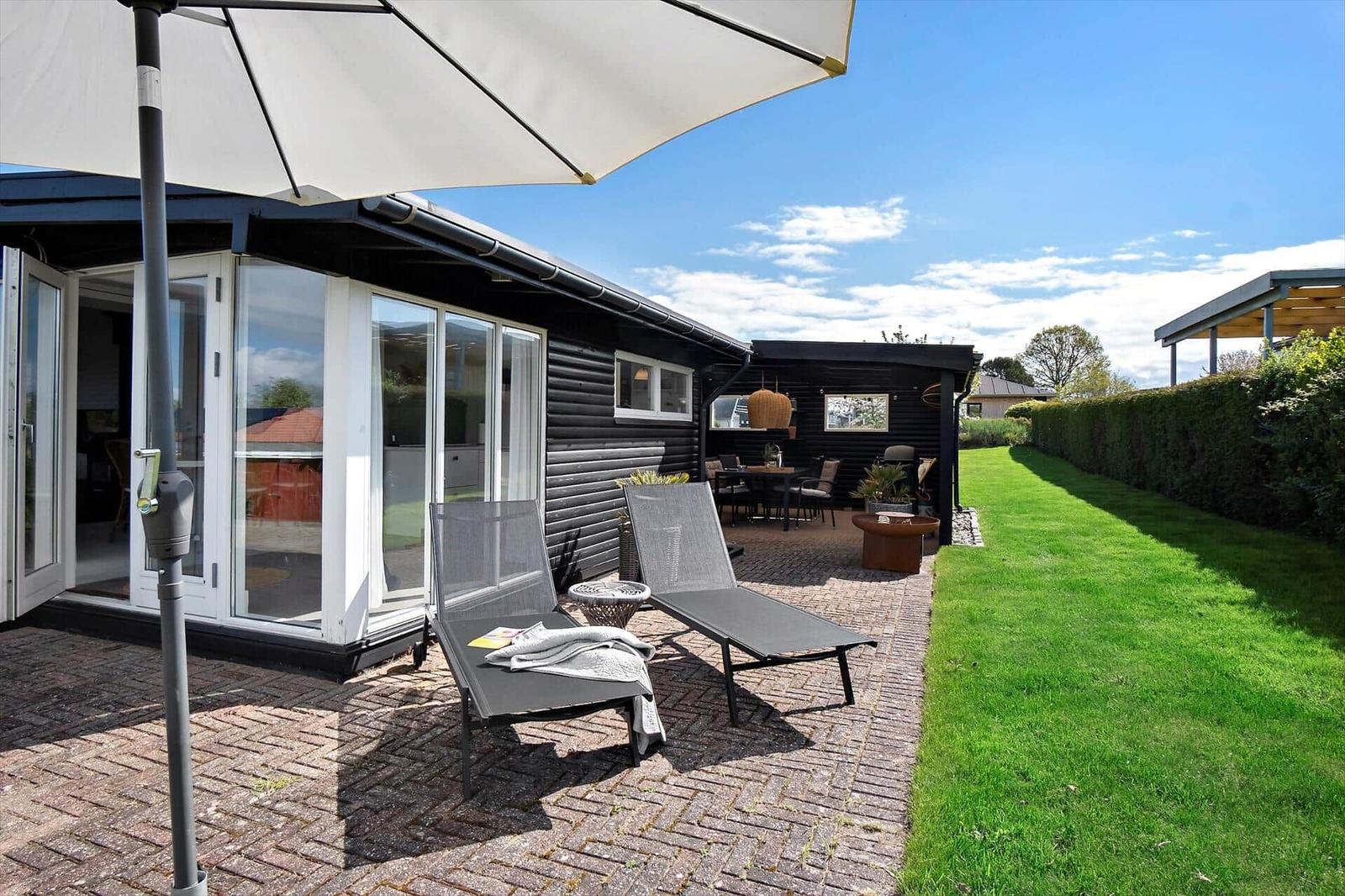 Terrasse mit Liegen, Sonnenschirm und Blick auf den Garten.